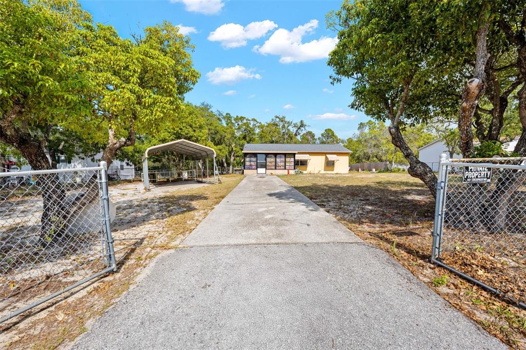 A concrete driveway leads to a single-story house with a carport and chain-link fencing — 17322 HARMONY DRIVE, HUDSON, FL