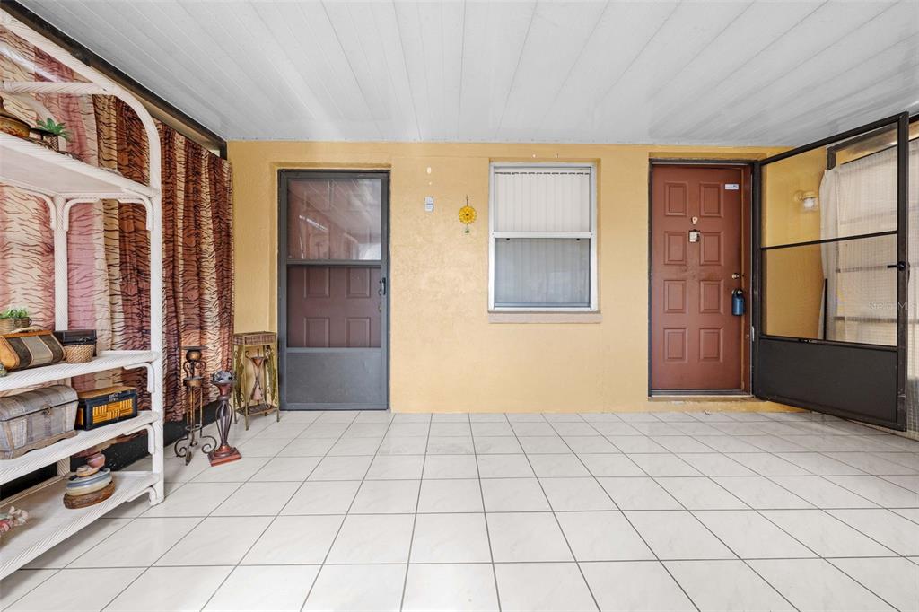 A covered patio features white tile flooring, yellow walls, a window, and two entry doors — 17322 HARMONY DRIVE, HUDSON, FL