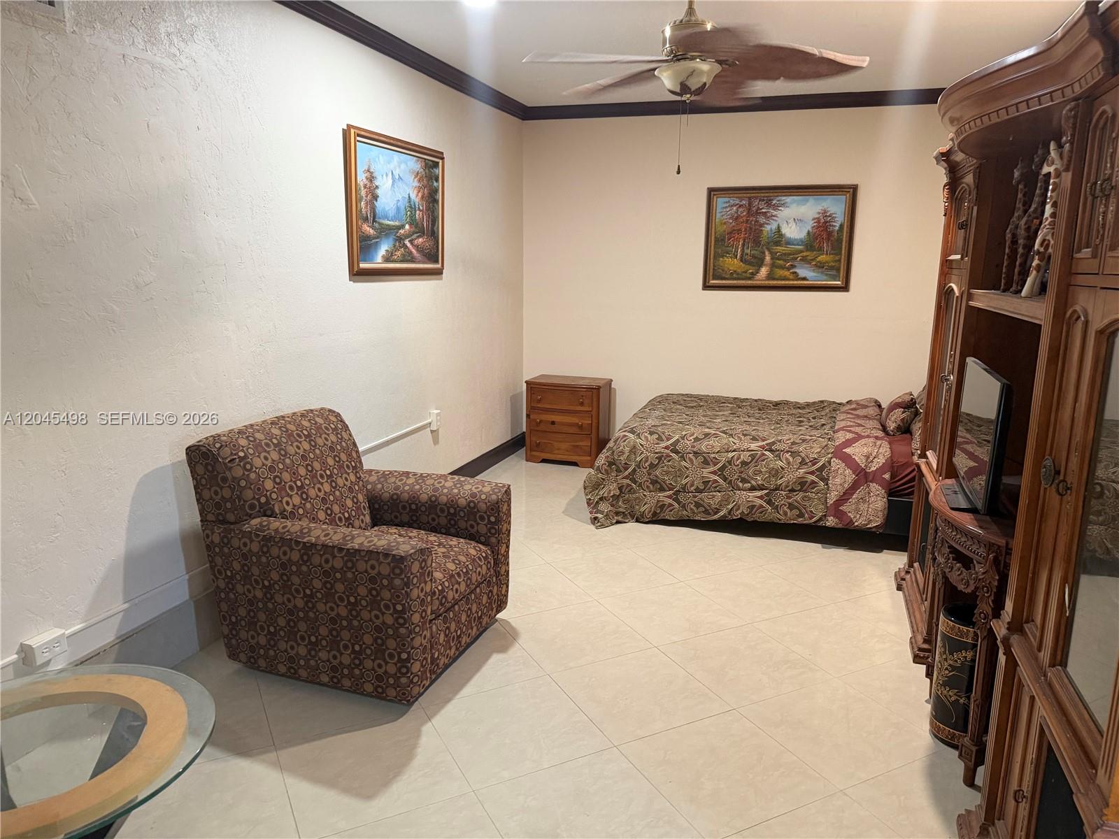 A bedroom features a patterned armchair, a bed, a wooden dresser, and a large armoire — MIRAMAR, FL