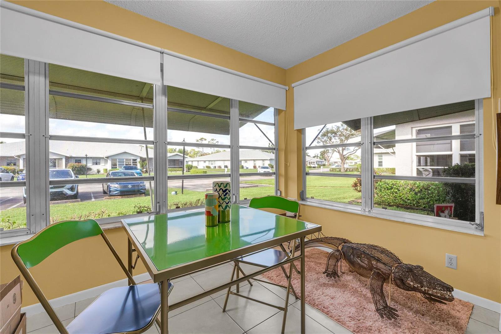 A sunroom with yellow walls, tile flooring, a green table, and a metal alligator sculpture — 14620 Canalview Drive # C, Delray Beach FL 33484, DELRAY BEACH, FL