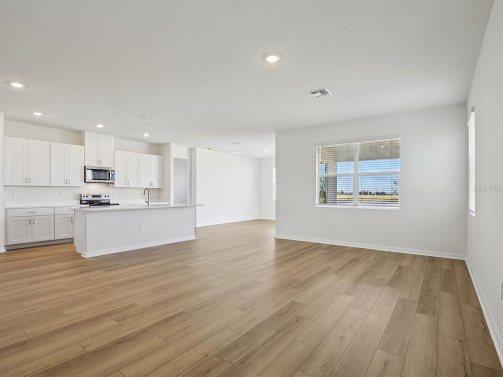 An open-concept kitchen and living area featuring white cabinets, light wood flooring, and large windows — 13220 SHELLMORE AVENUE, PALMETTO, FL