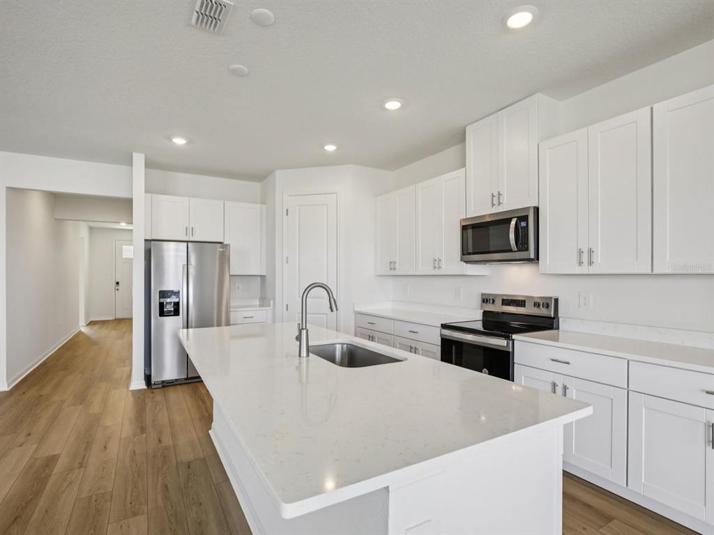 A modern kitchen features white cabinets, stainless steel appliances, and a large quartz-topped island — 13220 SHELLMORE AVENUE, PALMETTO, FL