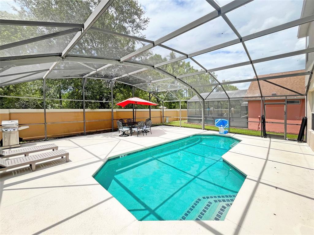 A screened-in patio features a swimming pool, lounge chairs, and a dining set with umbrella — 120 MADIERA BEACH BOULEVARD, KISSIMMEE, FL