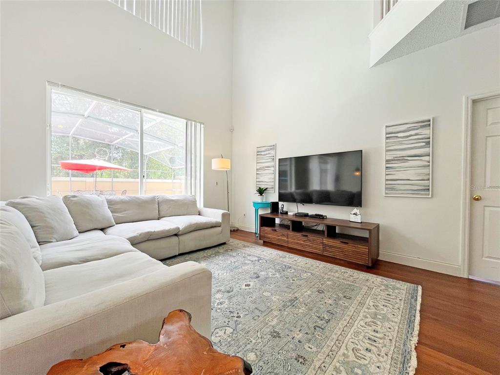 A living room features a high ceiling, a large sectional sofa, and a wall-mounted television — 120 MADIERA BEACH BOULEVARD, KISSIMMEE, FL