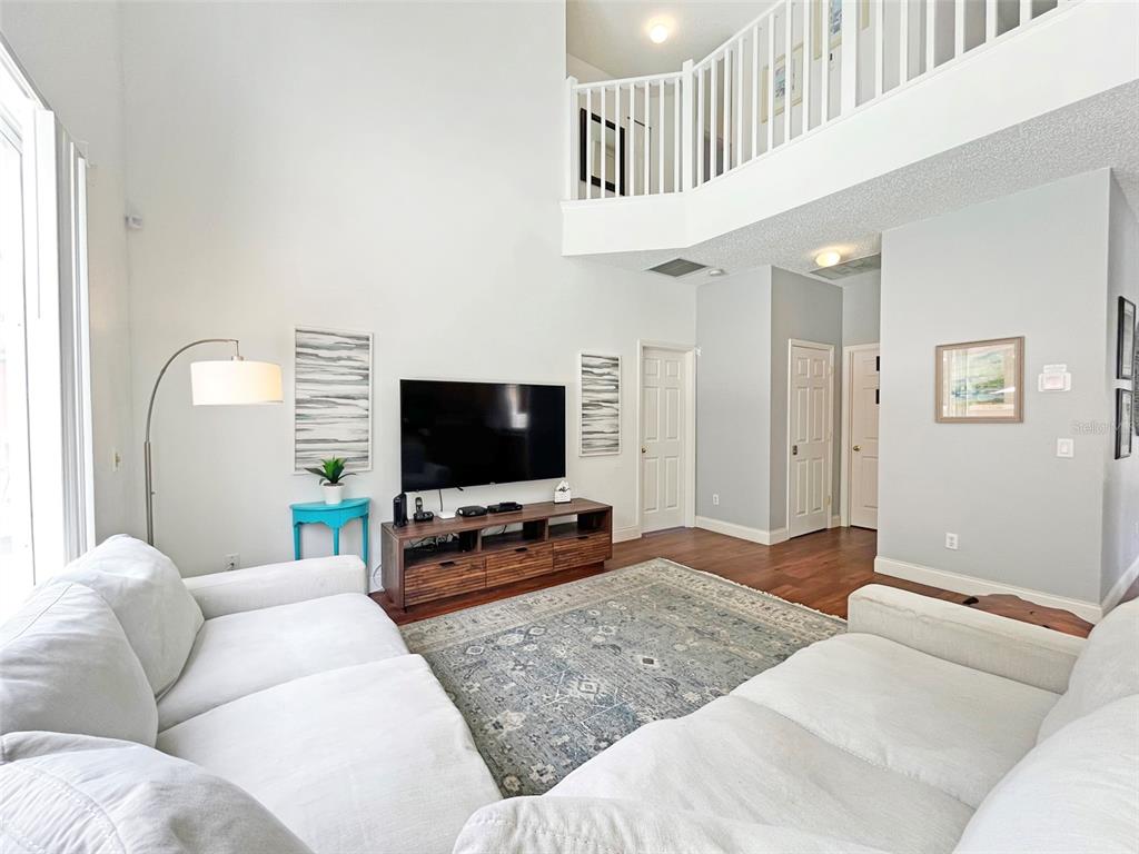 A living room with high ceilings, white sofas, a television console, and a lofted balcony — 120 MADIERA BEACH BOULEVARD, KISSIMMEE, FL