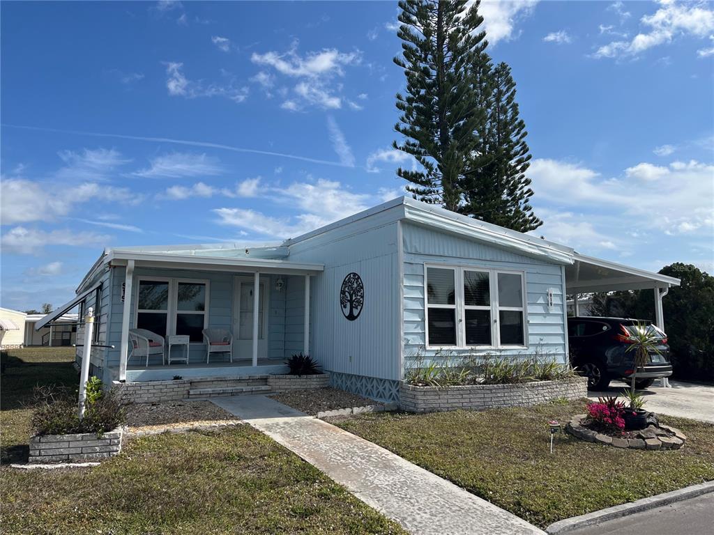 A light blue mobile home features a front porch, a carport, and a concrete walkway — 919 CORTINA BOULEVARD, VENICE, FL