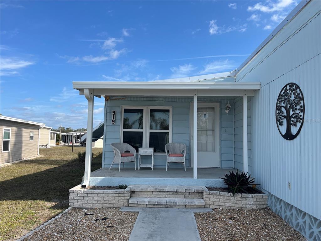 A light blue mobile home features a covered front porch with two chairs and steps — 919 CORTINA BOULEVARD, VENICE, FL