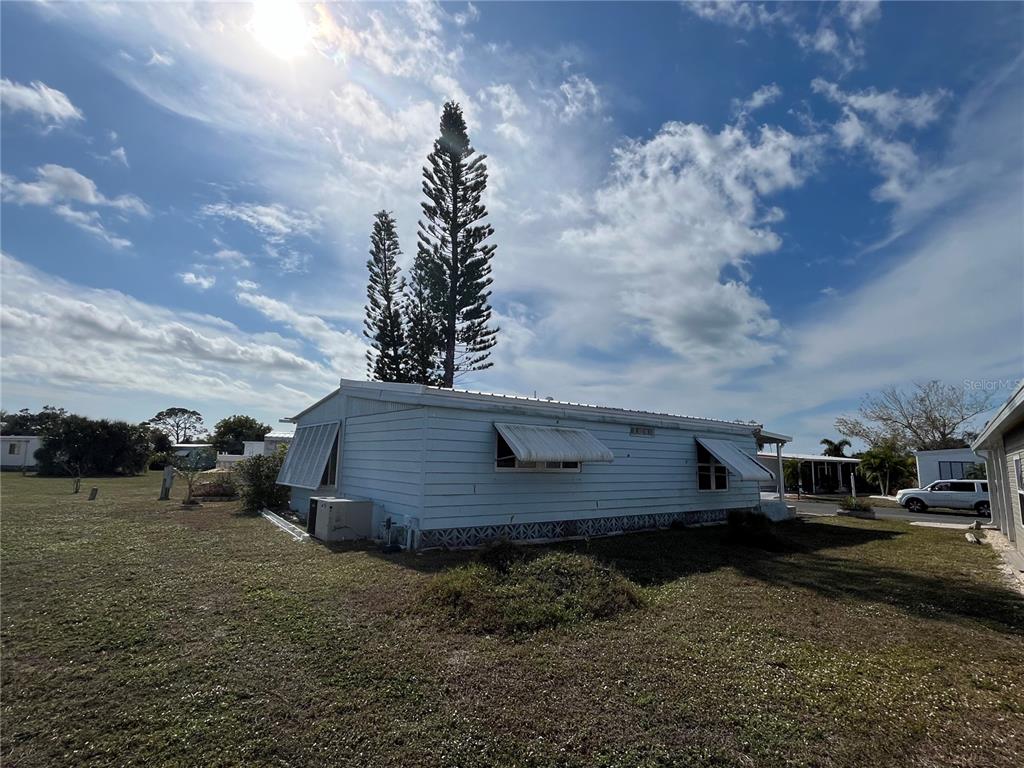 A light blue mobile home sits on a grassy lot under a cloudy sky — 919 CORTINA BOULEVARD, VENICE, FL