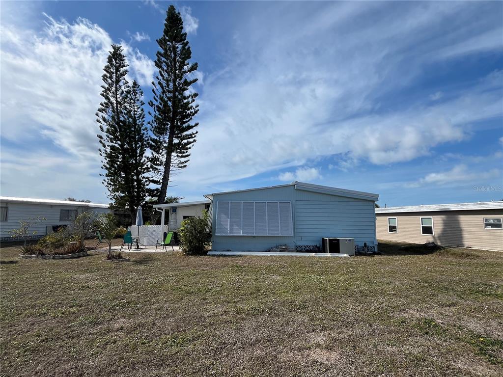 A light blue mobile home sits on a grassy lot with two tall pine trees — 919 CORTINA BOULEVARD, VENICE, FL