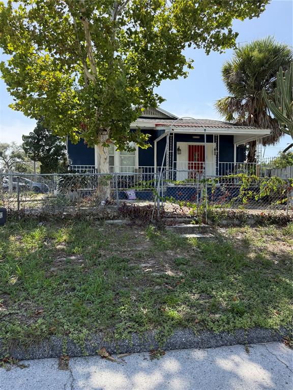 A blue house with a front porch and a large tree stands behind a chain-link fence — 3012 N ALBANY AVENUE, TAMPA, FL