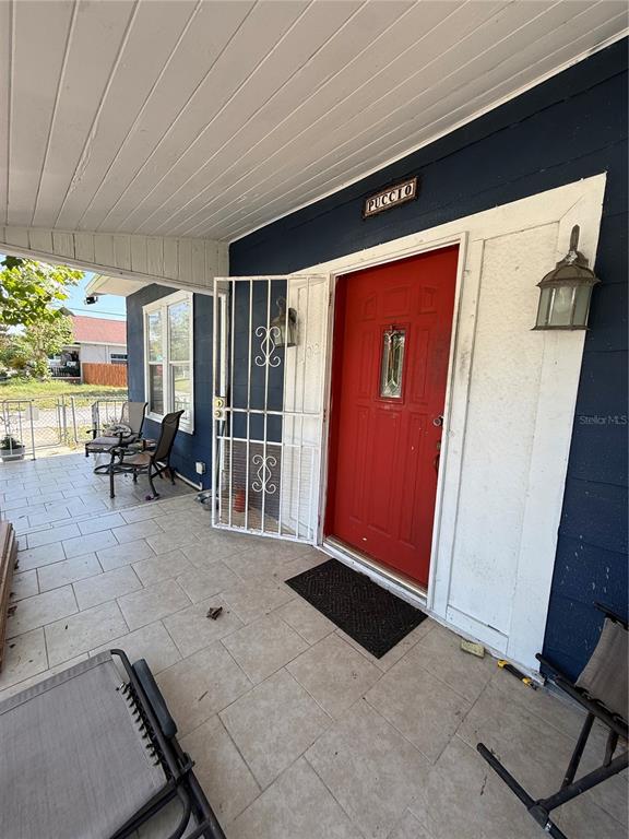 A covered porch features light-colored tile flooring, a red front door, and a security gate — 3012 N ALBANY AVENUE, TAMPA, FL