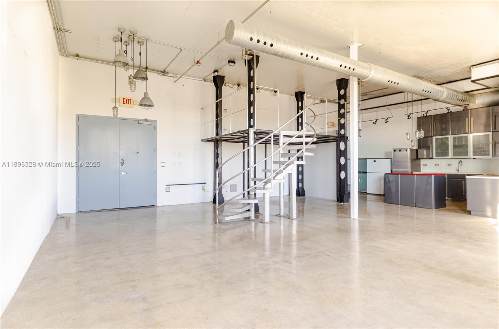An industrial-style open space features a spiral staircase, a metal loft, and a kitchen area — 250 NW 23 # 405, Miami FL 33127, MIAMI, FL