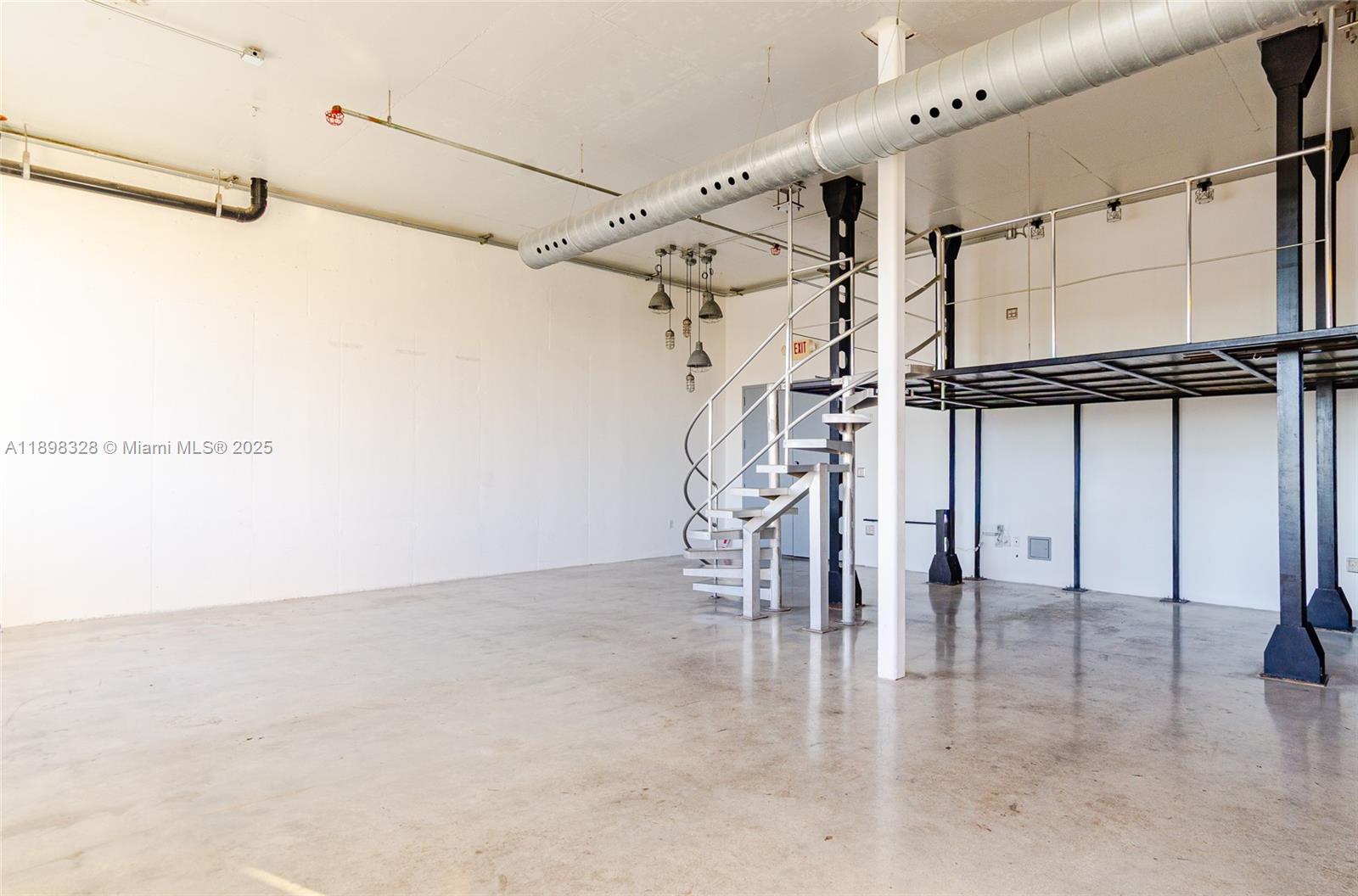 An industrial-style room features a concrete floor, a spiral staircase, and an elevated metal mezzanine — 250 NW 23 # 405, Miami FL 33127, MIAMI, FL