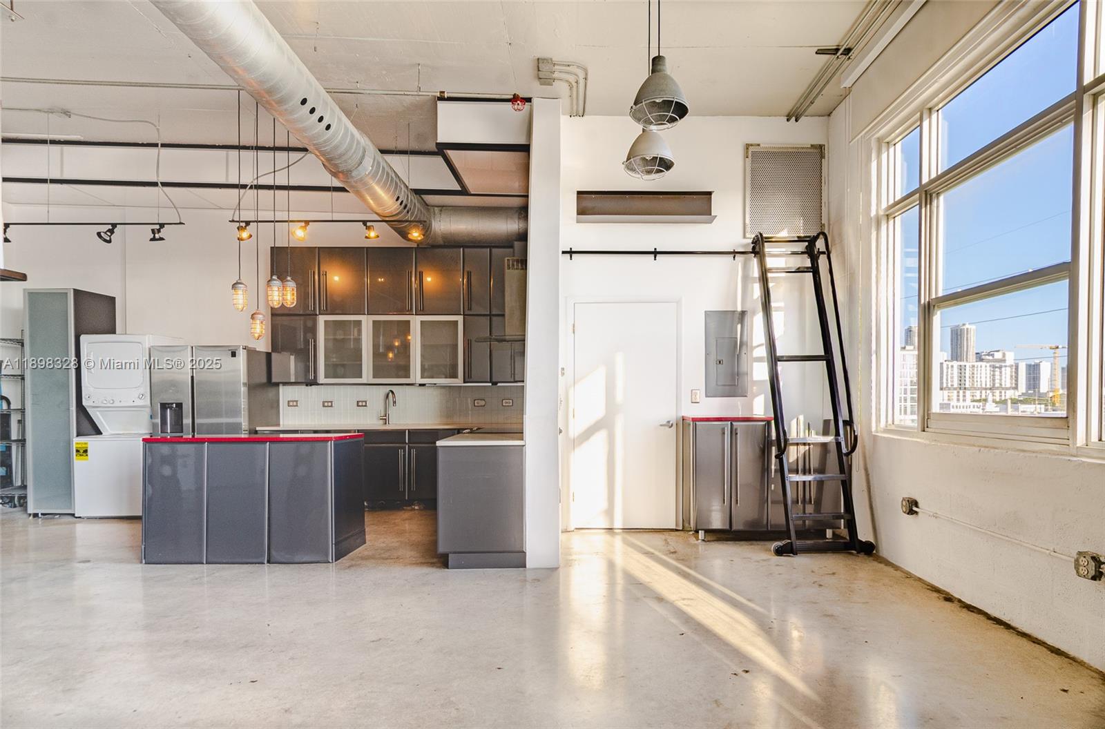 An industrial-style kitchen features grey cabinetry, a red-trimmed island, concrete floors, and a rolling ladder — 250 NW 23 # 405, Miami FL 33127, MIAMI, FL