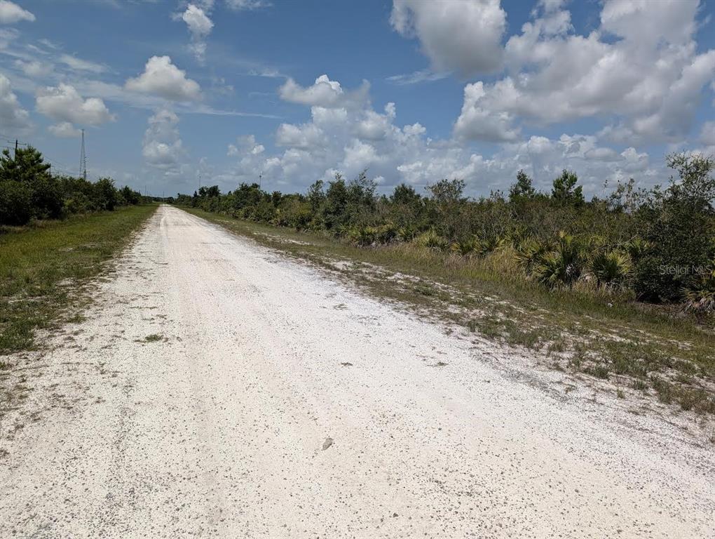 A long, unpaved white dirt road stretches through a rural landscape under a cloudy sky — ST PETERSBURG DRIVE, INDIAN LAKE ESTATES, FL