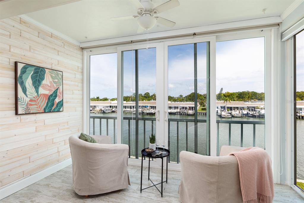 A sunroom with light wood-look flooring, two armchairs, and sliding glass doors overlooking a marina — 1 S BOCA CIEGA POINT BOULEVARD UNIT 204, ST PETERSBURG, FL