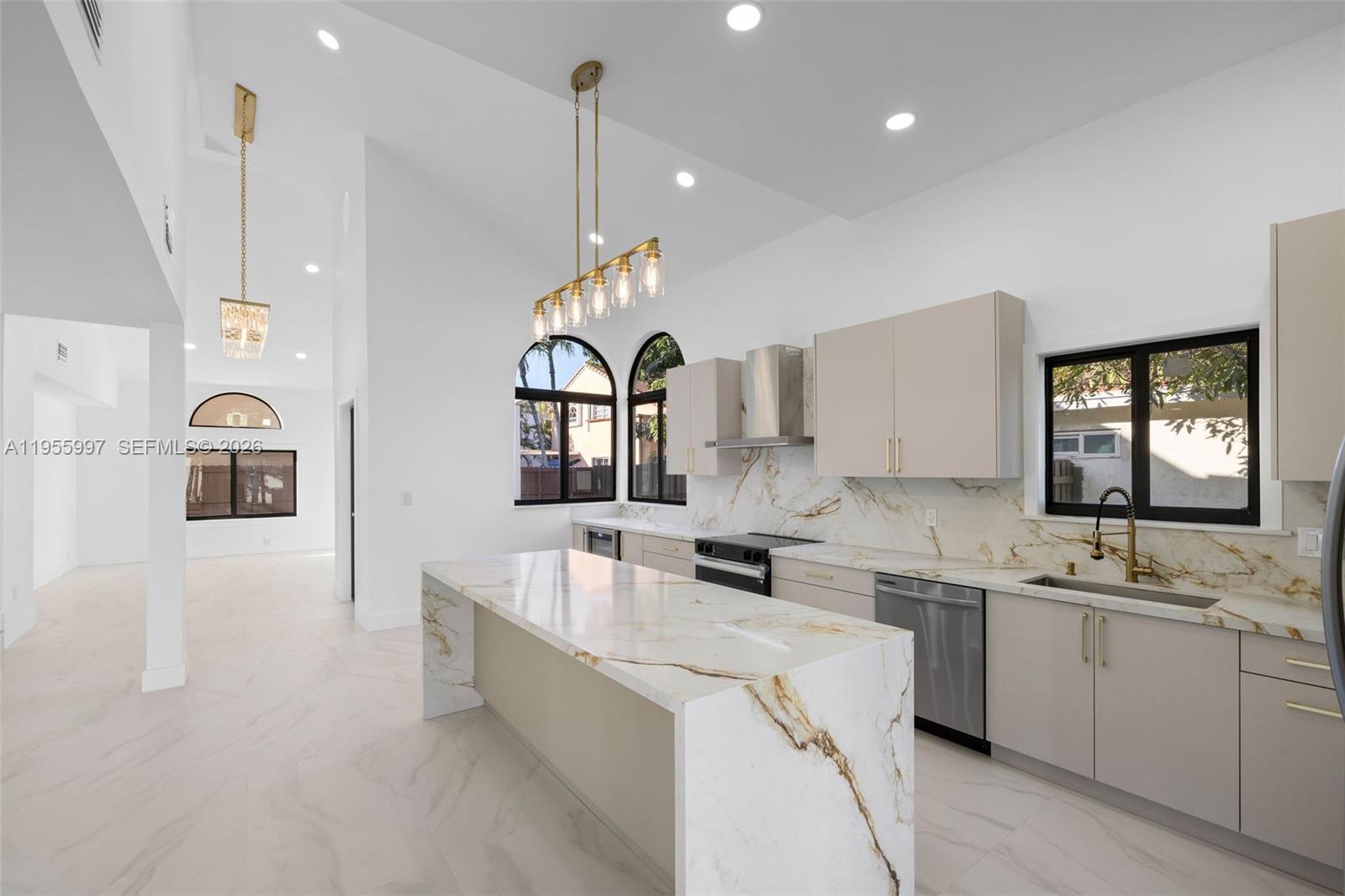 A modern kitchen features a marble waterfall island, light cabinetry, and gold light fixtures — 11260 SW 157th Ct, Miami FL 33196, MIAMI, FL