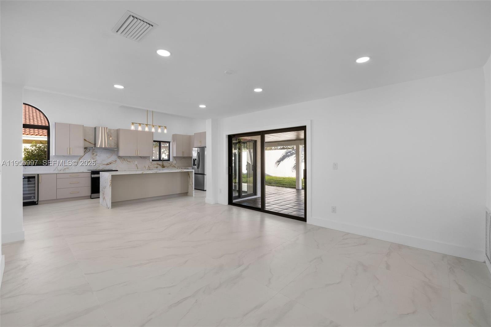 A modern open-concept kitchen and living area features white marble floors and sliding glass doors — 11260 SW 157th Ct, Miami FL 33196, MIAMI, FL