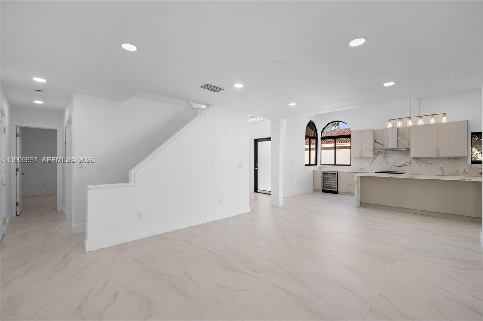 A modern kitchen and living area feature white marble-look flooring, beige cabinetry, and arched windows — 11260 SW 157th Ct, Miami FL 33196, MIAMI, FL