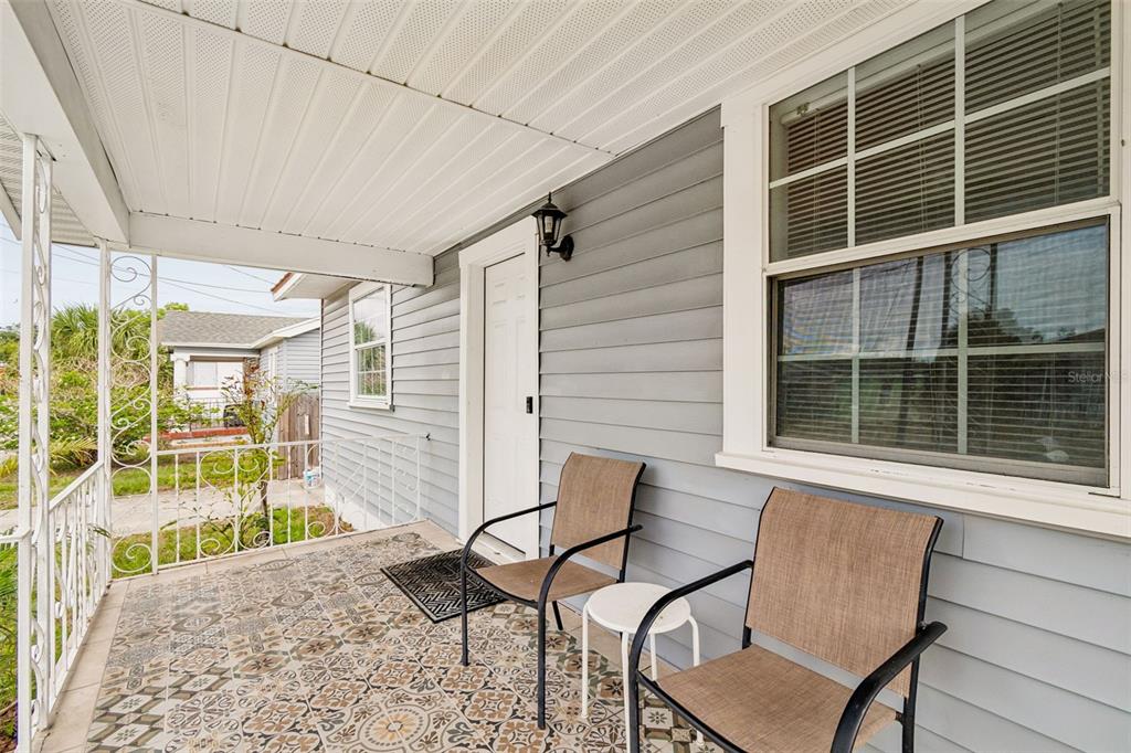 A covered front porch features patterned tile flooring, gray siding, and two outdoor chairs — 1406 E 23RD AVENUE, TAMPA, FL