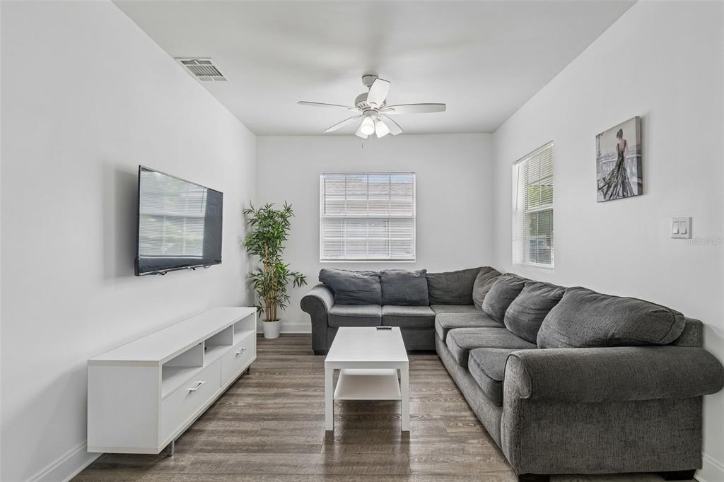 A living room features a grey sectional sofa, white media console, and wood-look flooring — 1406 E 23RD AVENUE, TAMPA, FL