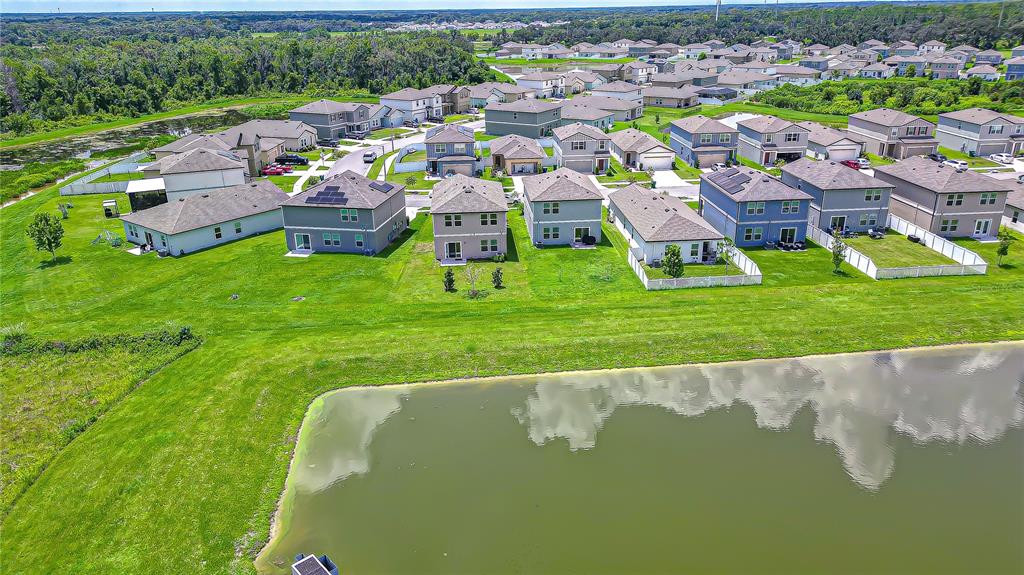 An aerial view shows a suburban neighborhood with houses surrounding a retention pond — 35651 BUTTONWEED TRAIL, ZEPHYRHILLS, FL