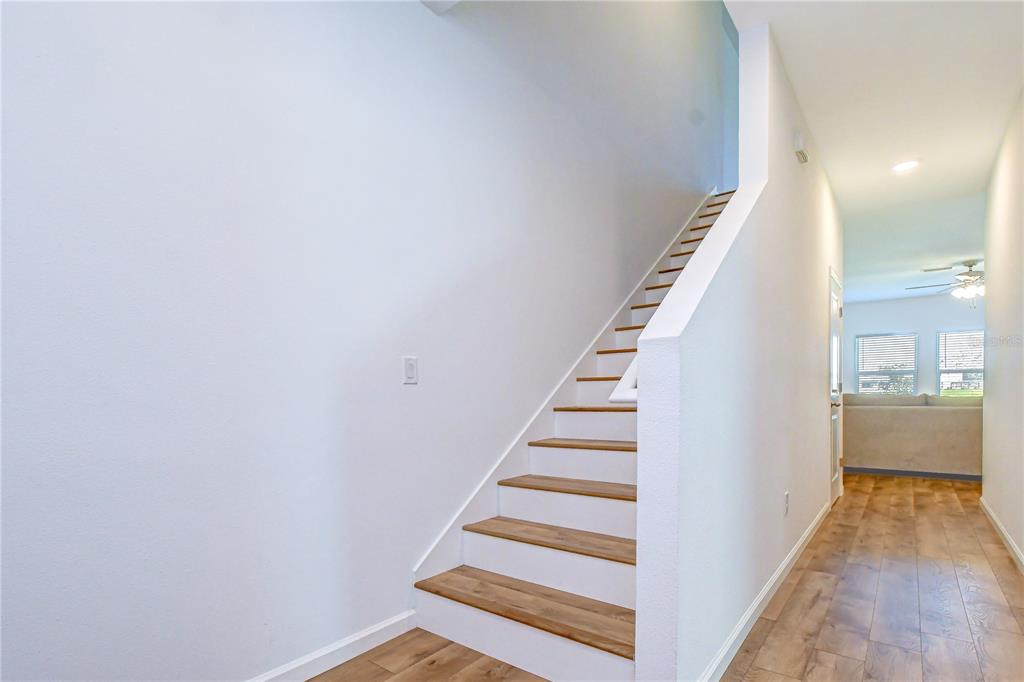 A staircase with wooden treads and white risers sits beside a hallway with wood flooring — 35651 BUTTONWEED TRAIL, ZEPHYRHILLS, FL