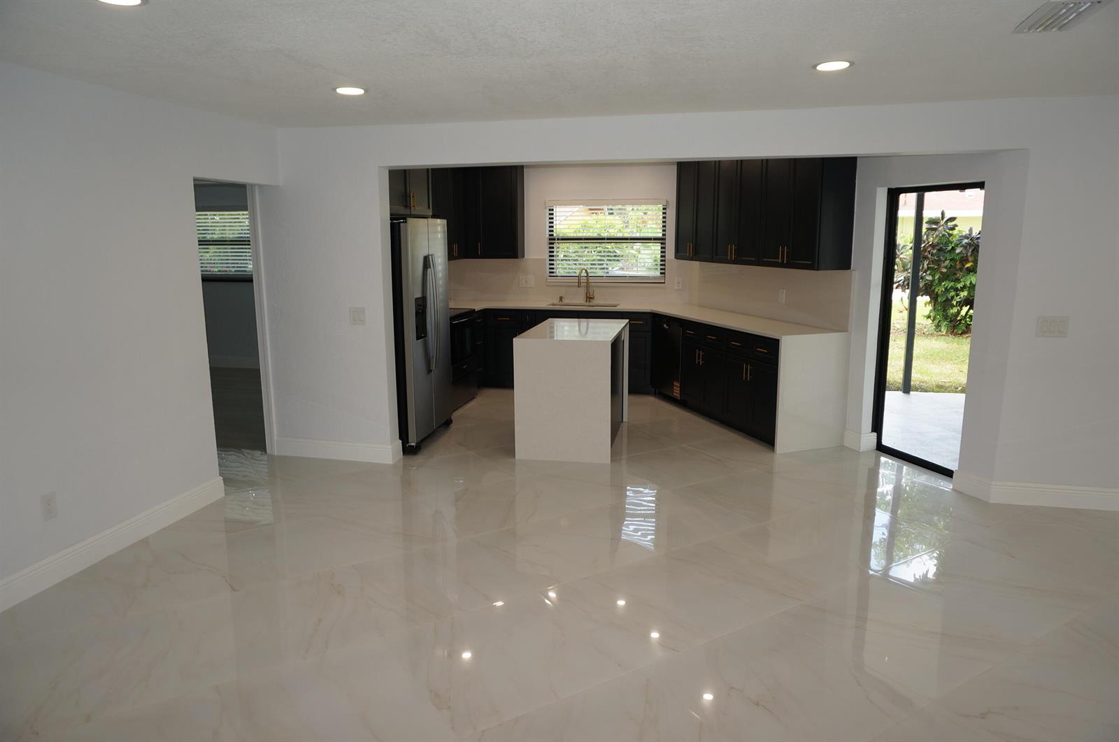A modern kitchen features dark cabinets, white countertops, a central island, and polished tile floors — 1513 39th Street, West Palm Beach FL 33407, WEST PALM BEACH, FL