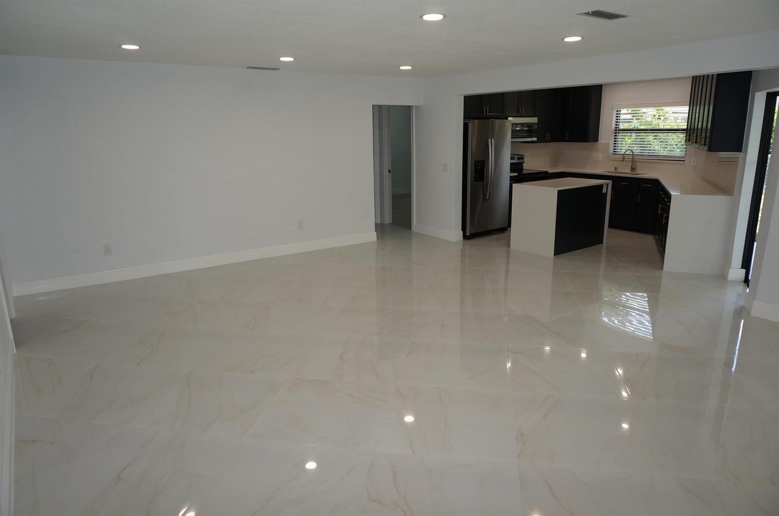 An open-concept living area features white marble-look tile flooring and an adjacent modern kitchen — 1513 39th Street, West Palm Beach FL 33407, WEST PALM BEACH, FL