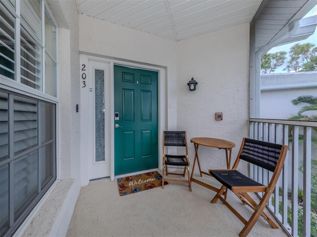 A teal front door with a welcome mat and patio furniture on a covered porch — 901 ADDINGTON COURT UNIT 203, VENICE, FL