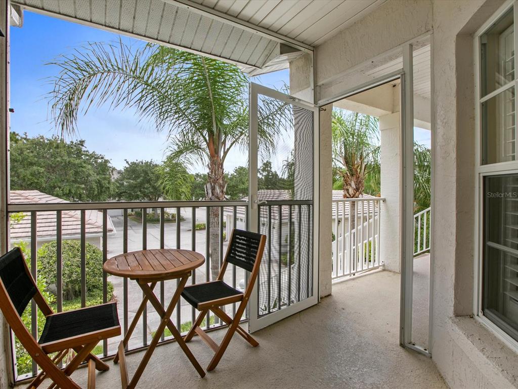 A balcony features a small wooden table, two chairs, and a screen door — 901 ADDINGTON COURT UNIT 203, VENICE, FL