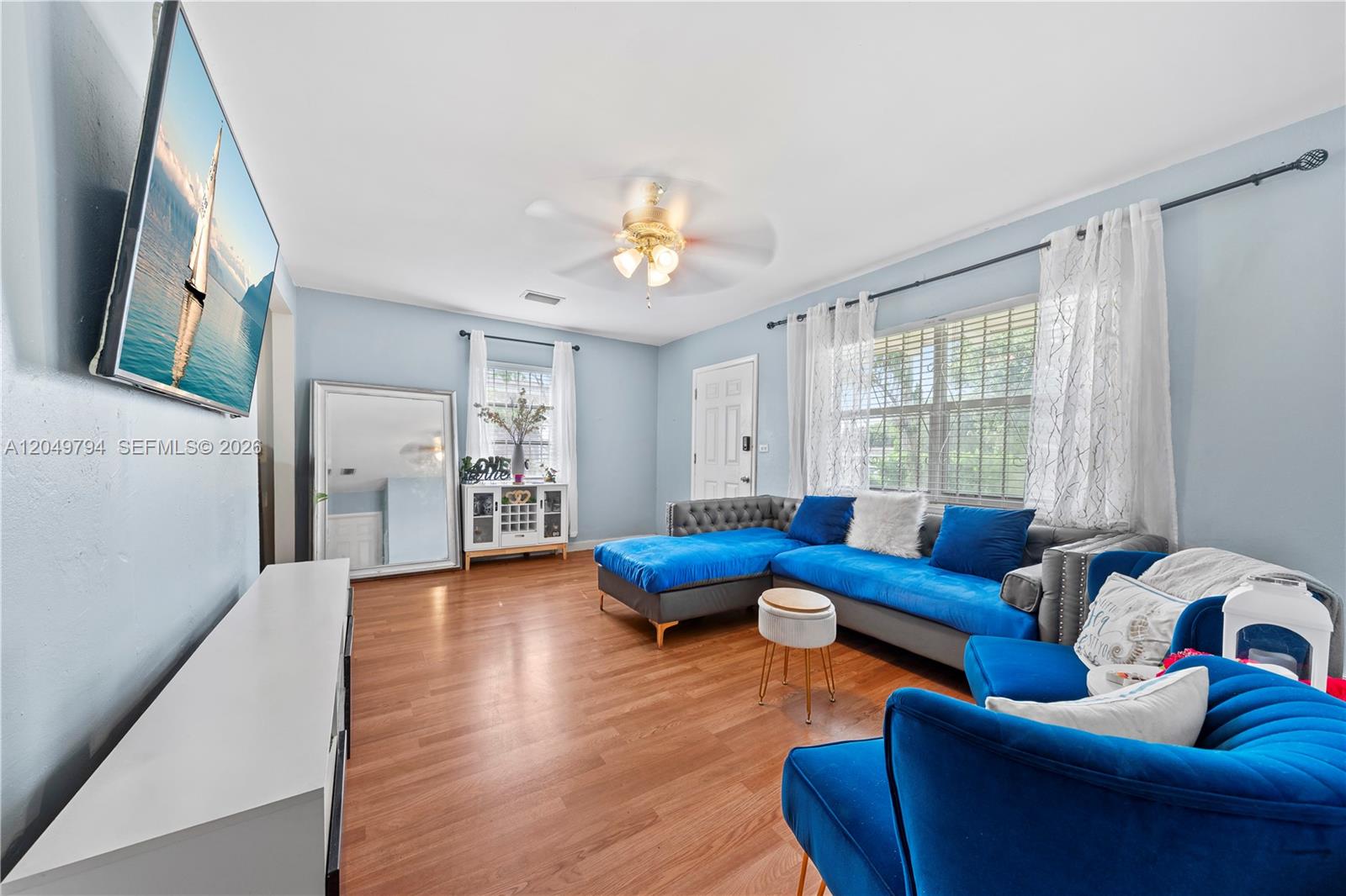 A living room features light blue walls, hardwood floors, a blue sectional, and a television — 1920 NW 69th Ter, Miami FL 33147, MIAMI, FL