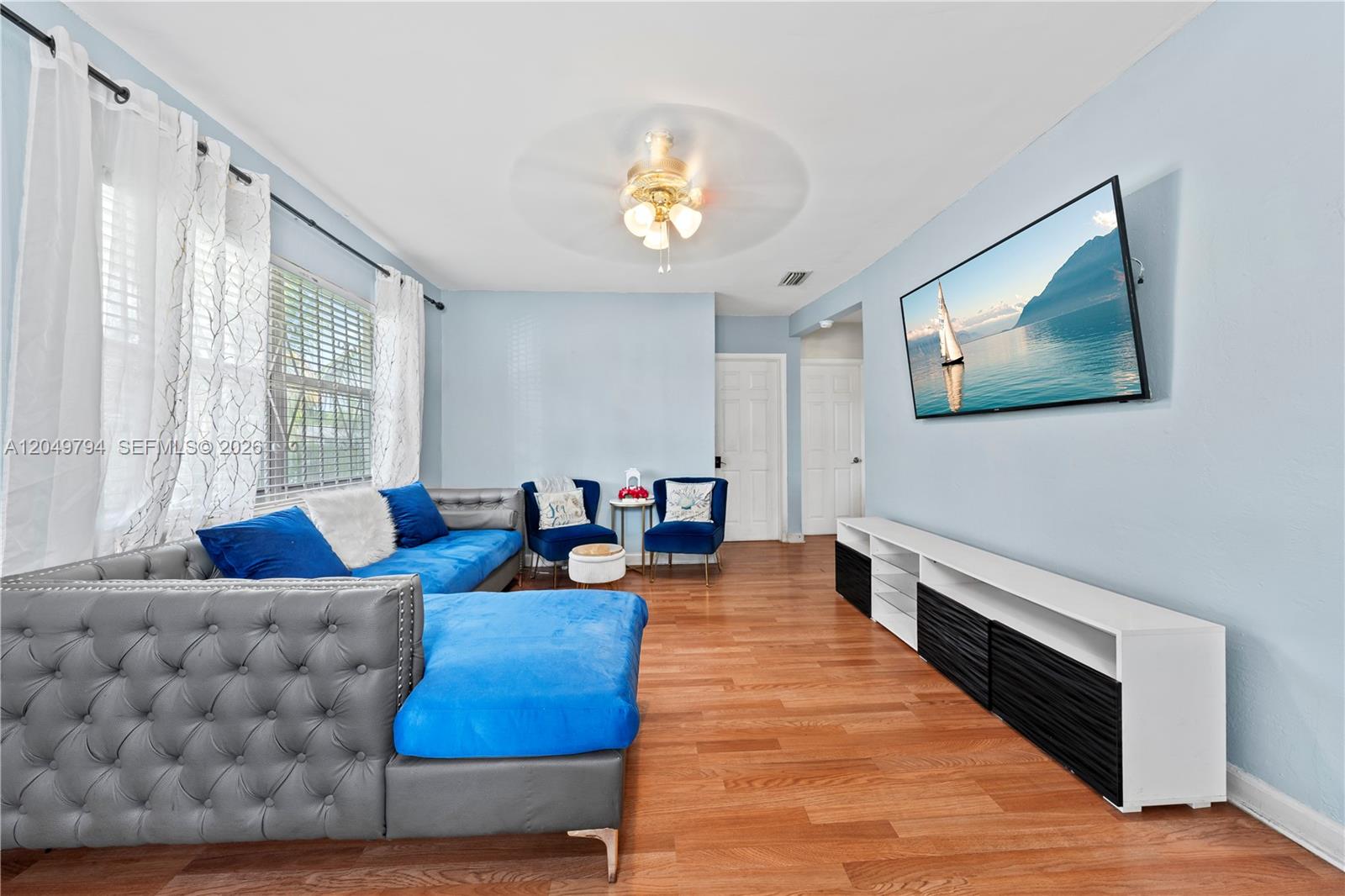 A living room features a blue sectional, two armchairs, a television, and hardwood flooring — 1920 NW 69th Ter, Miami FL 33147, MIAMI, FL