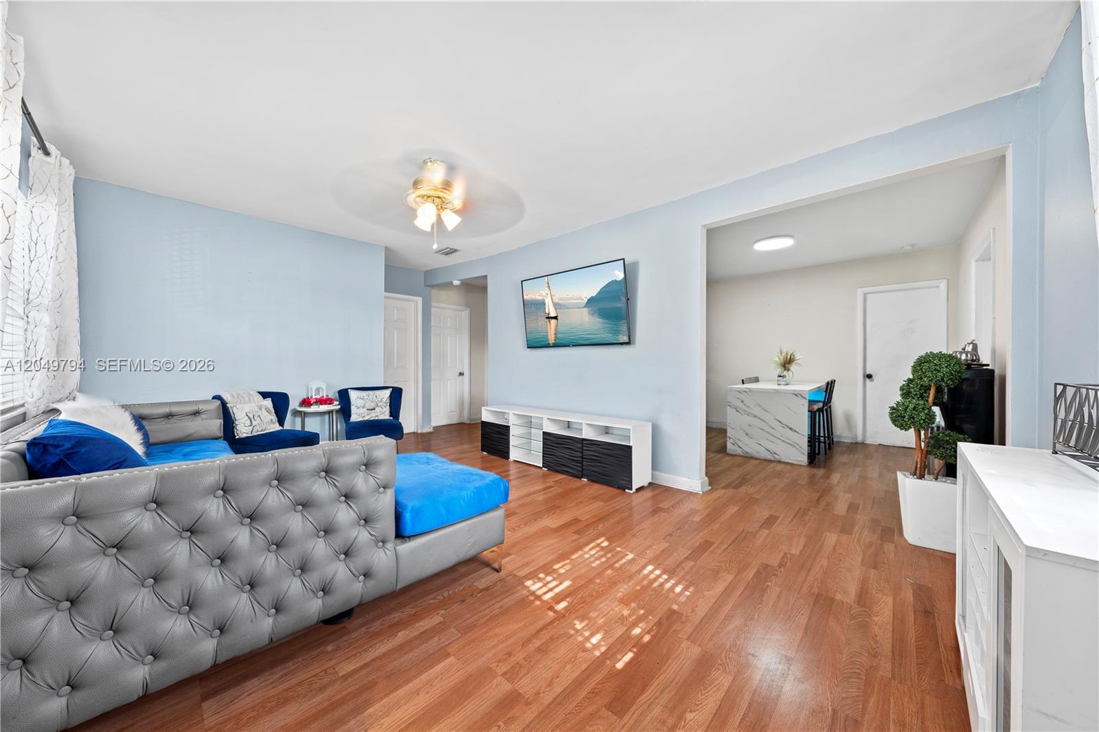 A living room with blue walls, a tufted gray sofa, and an adjacent dining area — 1920 NW 69th Ter, Miami FL 33147, MIAMI, FL