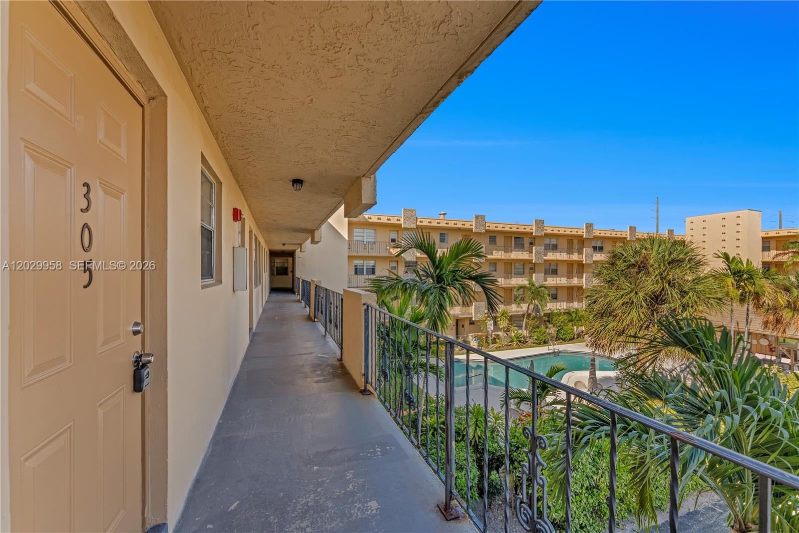 An outdoor walkway overlooks a swimming pool and apartment complex under a clear blue sky — 2145 Pierce St # 305, Hollywood FL 33020, HOLLYWOOD, FL