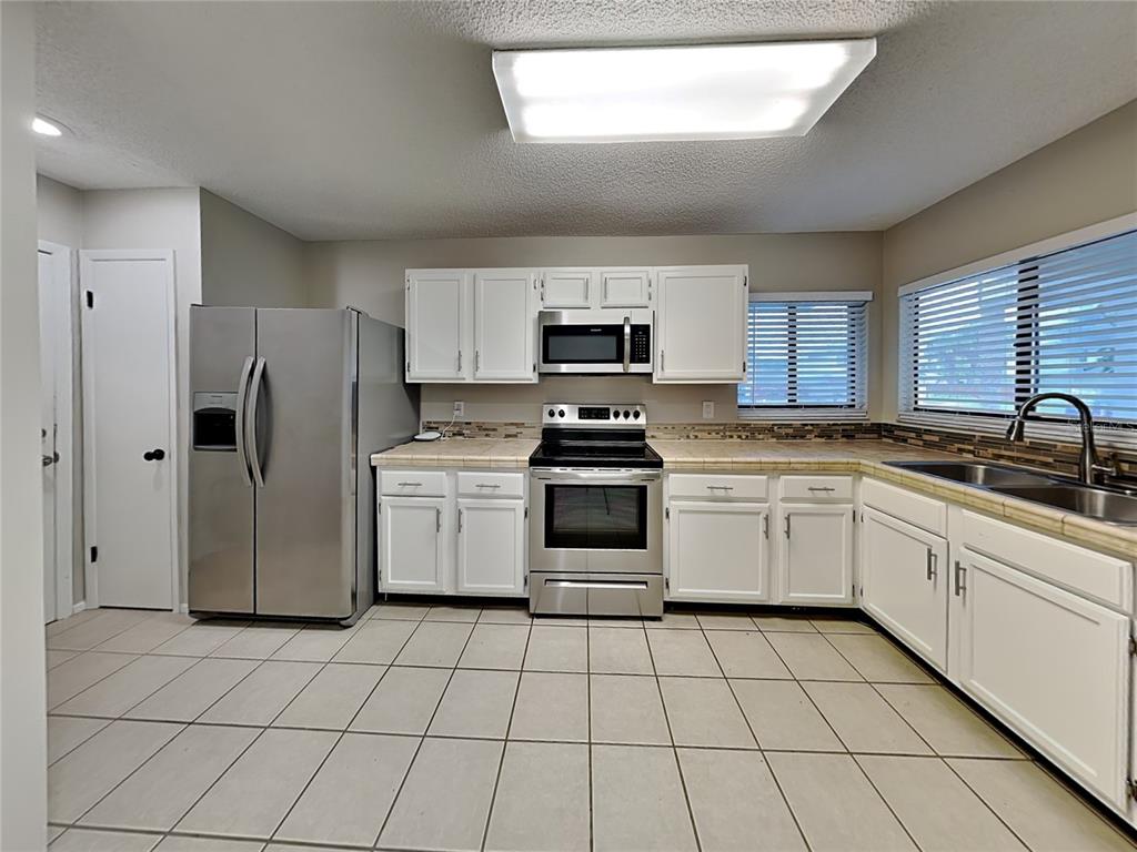 A kitchen features white cabinets, stainless steel appliances, tiled countertops, and light-colored floor tiles — 419 E SPRINGTREE WAY, LAKE MARY, FL
