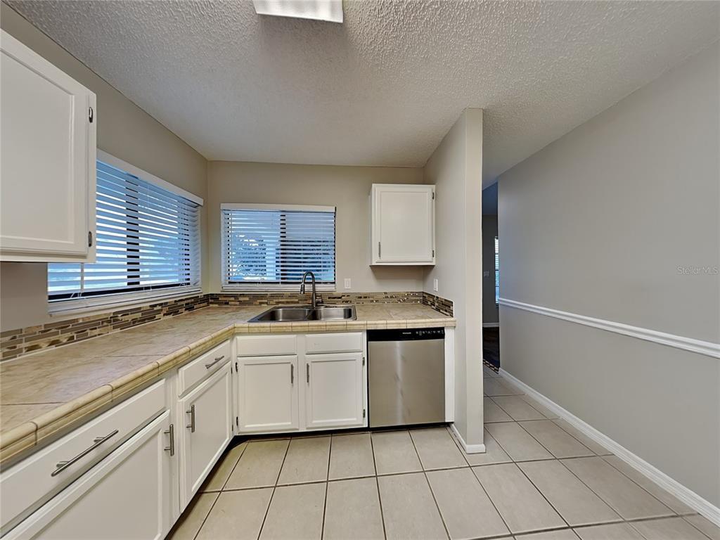 A kitchen features white cabinets, tiled countertops, a stainless steel dishwasher, and tile flooring — 419 E SPRINGTREE WAY, LAKE MARY, FL