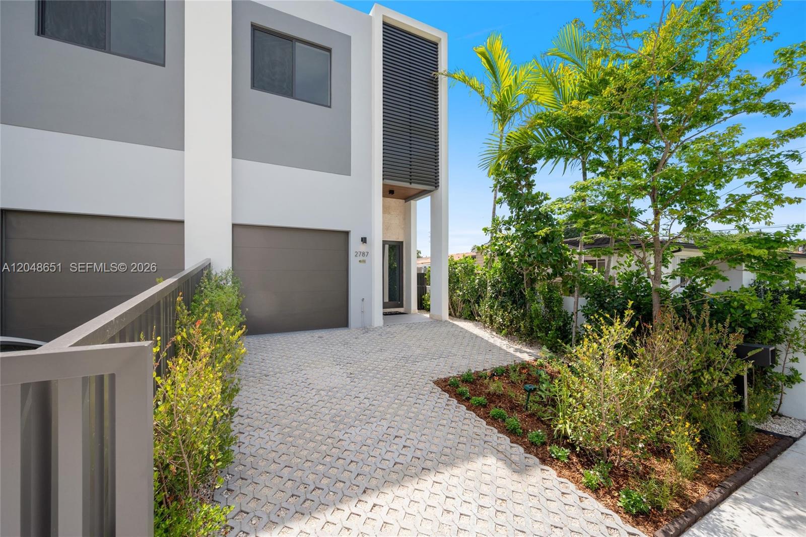 A modern two-story townhouse features a gray garage, a paved driveway, and lush landscaping — 2787 SW 34th Ave, Miami FL 33133, MIAMI, FL