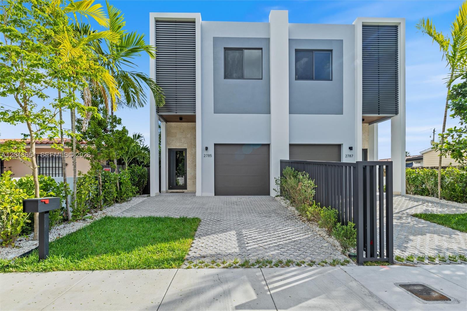 A modern two-story duplex features gray garage doors, stone accents, and a paved driveway — 2787 SW 34th Ave, Miami FL 33133, MIAMI, FL