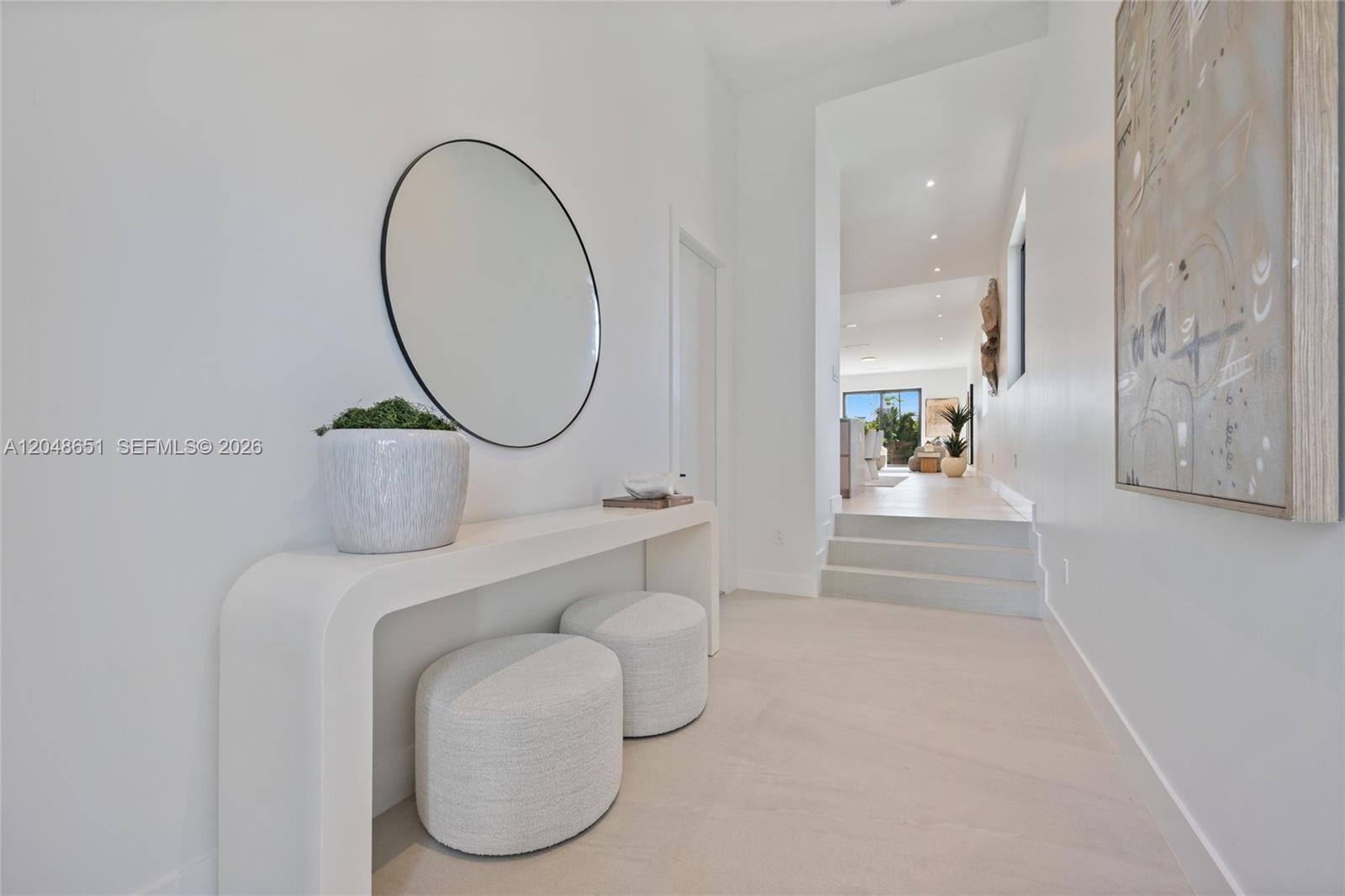 A white hallway features a console table, round mirror, two ottomans, and steps leading upward — 2787 SW 34th Ave, Miami FL 33133, MIAMI, FL