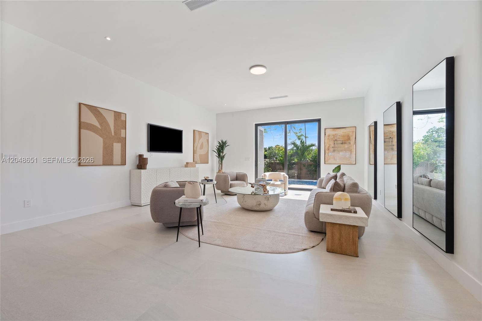 A bright living room features neutral furniture, a round rug, and large sliding glass doors — 2787 SW 34th Ave, Miami FL 33133, MIAMI, FL