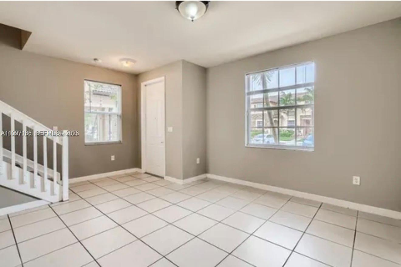 An empty room with light-colored tile flooring, gray walls, a staircase, and two windows — 9125 SW 227th St # 1, Cutler Bay FL 33190, CUTLER BAY, FL