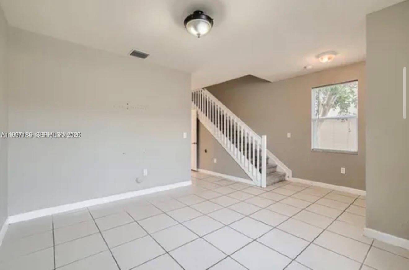 An empty room with light-colored tile flooring, a staircase with white railings, and beige walls — 9125 SW 227th St # 1, Cutler Bay FL 33190, CUTLER BAY, FL