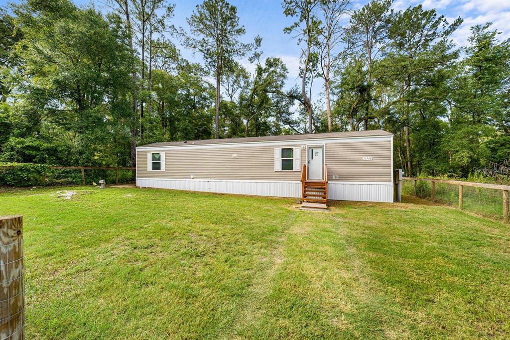 A single-story manufactured home with tan siding sits on a grassy lot near trees — 11776 NW 21ST STREET, OCALA, FL