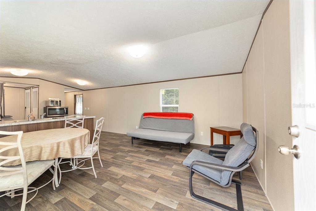 A living room and dining area with wood-look flooring, a futon, and a small table — 11776 NW 21ST STREET, OCALA, FL