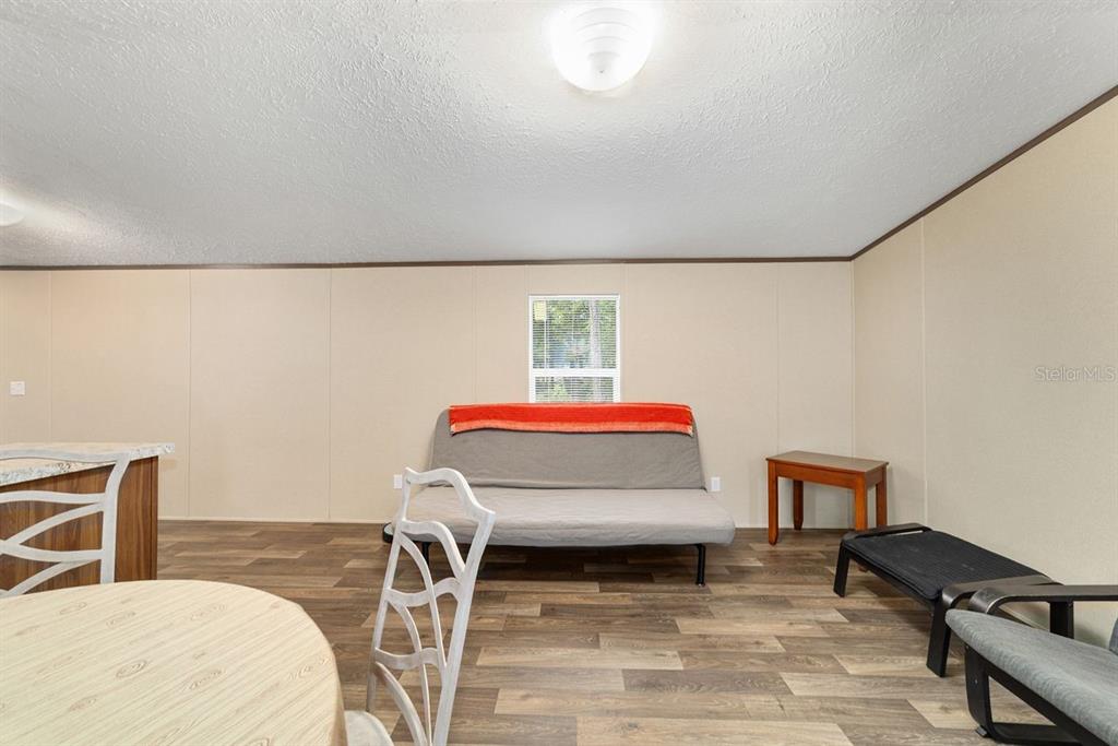 A living area features wood-look flooring, a gray futon with an orange throw, and a window — 11776 NW 21ST STREET, OCALA, FL
