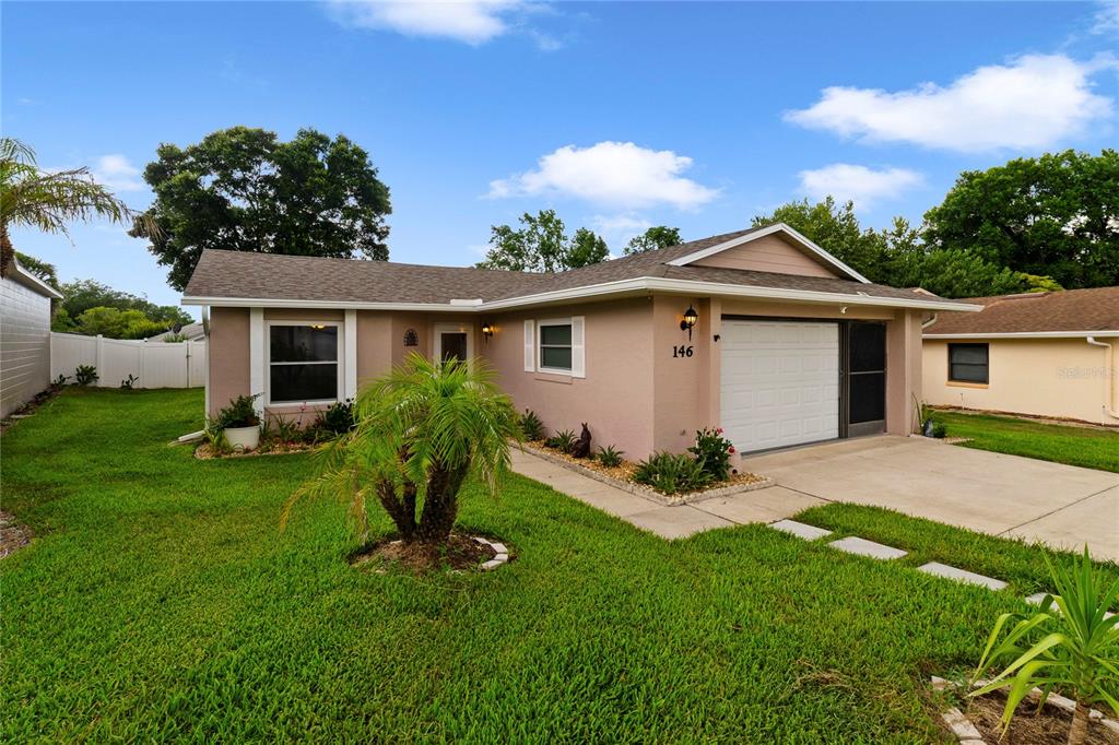 A single-story house with a tan exterior, a white garage door, and a front lawn — 146 MAYFAIR COURT, SANFORD, FL