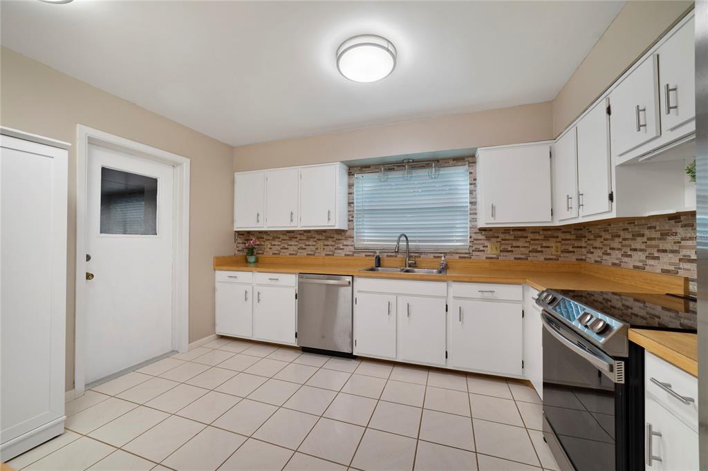 A kitchen features white cabinets, wood countertops, stainless steel appliances, and light-colored tile flooring — 146 MAYFAIR COURT, SANFORD, FL