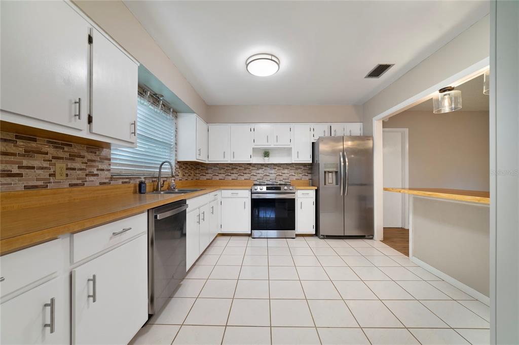A kitchen features white cabinets, wood-look countertops, stainless steel appliances, and white tile flooring — 146 MAYFAIR COURT, SANFORD, FL