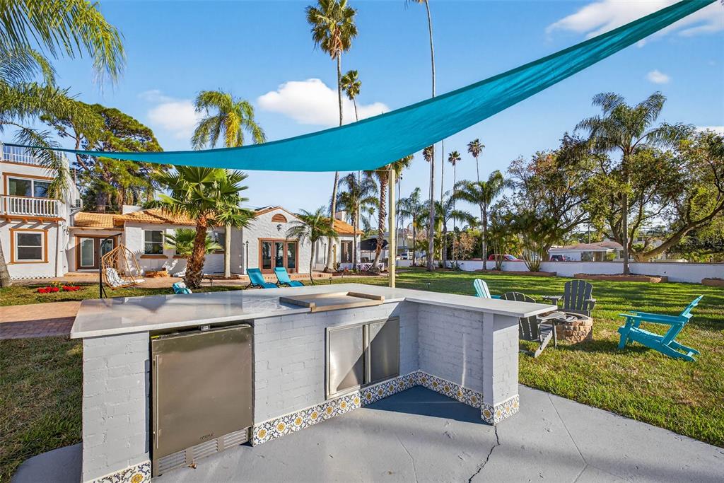 An outdoor kitchen with a stone countertop and stainless steel appliances sits under a shade sail — 236 SAN SALVADOR DRIVE, DUNEDIN, FL